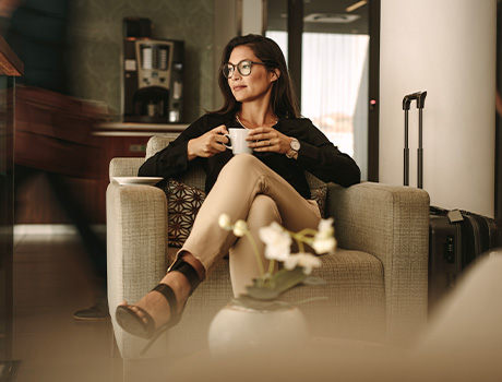 Donna elegante seduta mentre sorseggia un caffè con Carta Platino American Express in primo piano 